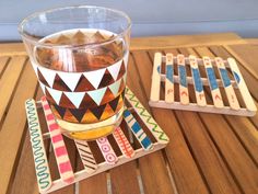 a glass filled with liquid sitting on top of a wooden coaster next to a cup