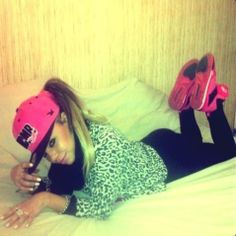 a young woman laying on top of a bed wearing a pink hat and holding a cell phone