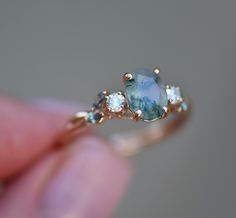 a woman's hand holding a ring with an aqua blue stone and three white diamonds