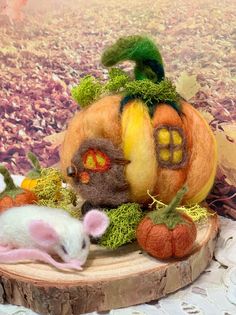 a small mouse sitting on top of a wooden stump next to a pumpkin and other decorations