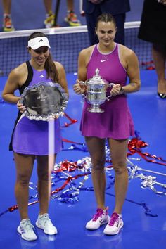 two female tennis players hold their trophies on the court