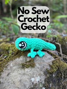 a small crocheted gecko sitting on top of a rock in the woods