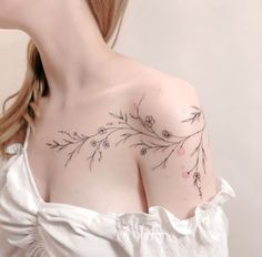 a woman wearing a white dress with flowers on her shoulder and chest tattooing it's upper half