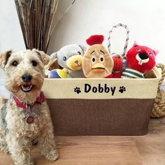 a dog is sitting next to a basket with stuffed animals in it that says dobby