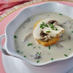 a white bowl filled with soup on top of a pink table cloth and silverware