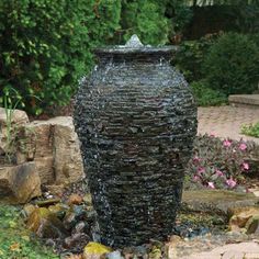 a large water fountain in the middle of a garden with rocks and plants around it