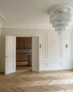 an empty room with white walls and wood floors, chandelier hanging from the ceiling