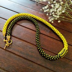 a yellow and black beaded necklace sitting on top of a wooden table next to flowers