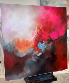 an abstract painting is displayed in front of a white background and red, pink, blue, and black clouds