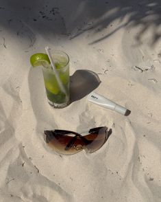 a drink and sunglasses sitting in the sand