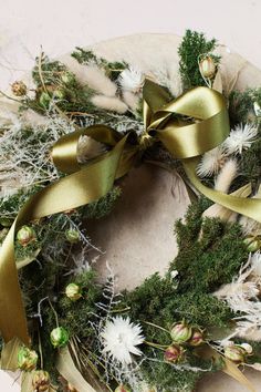 a wreath is adorned with green and white flowers, pine cones, and gold ribbon