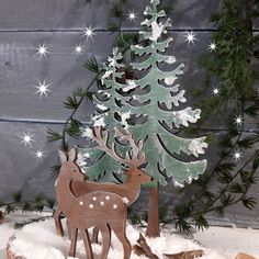 a christmas tree with two deer standing next to it on top of snow covered ground