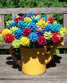 a yellow vase filled with colorful flowers sitting on top of a wooden bench