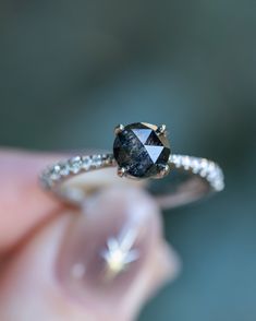 a close up of a person's hand holding a ring with a black diamond