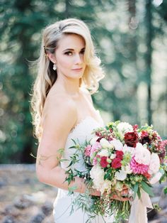 a woman in a wedding dress holding a bridal bouquet and looking at the camera