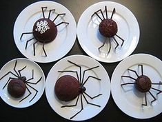 four white plates topped with chocolate desserts covered in spider web designs and sprinkles