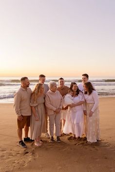 a group of people standing next to each other on top of a sandy beach near the ocean