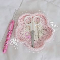 there is a crocheted heart with scissors and other items on it next to a pink pen