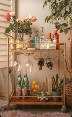 a bar cart filled with bottles and glasses on top of a wooden table next to a potted plant