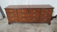 a wooden dresser with many drawers and knobs on the bottom drawer, in front of a white wall