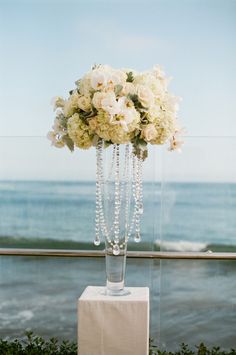 a vase filled with flowers sitting on top of a white table next to the ocean