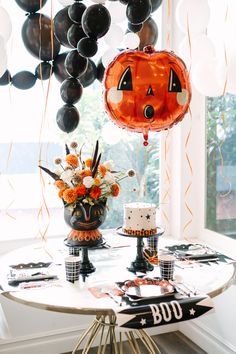 a halloween themed party with balloons, cake and decorations on a table in front of a window