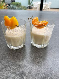 two glasses filled with oranges and cream on top of a granite countertop next to each other