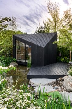 a small black house sitting on top of a lush green field next to a pond