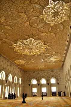 an ornate ceiling in the middle of a room with many windows and people standing around