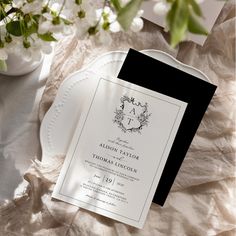 an elegant black and white wedding card on a plate with flowers in the vase behind it