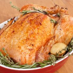 a close up of a chicken in a bowl with potatoes and herbs on the side