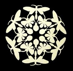 a circular design made out of white paper with leaves and flowers in the center on a black background