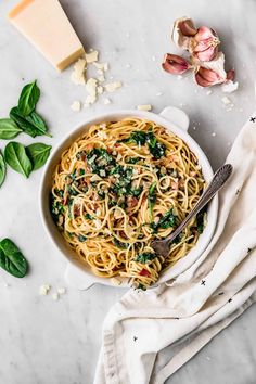 a bowl of pasta with spinach and parmesan cheese next to some garlic