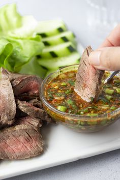 a person dipping some food into a bowl on top of a white plate with lettuce