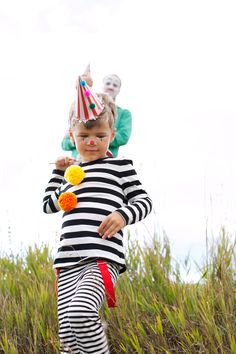 a little boy wearing a clown hat and striped shirt is playing with a ball in the grass