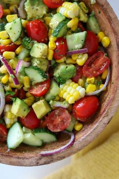 a salad with cucumbers, tomatoes, corn and avocado in a wooden bowl