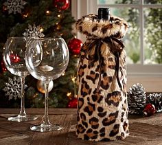 a wine bottle in a leopard print bag next to two wine glasses and a christmas tree