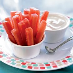 a small white bowl filled with watermelon sticks next to a cup of yogurt