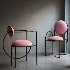 two pink chairs sitting next to each other in front of a gray wall and window