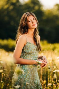 a beautiful young woman in a dress standing in a field with tall grass and wildflowers