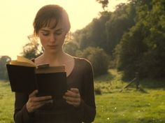 a woman is reading a book in the grass with trees in the backgroud