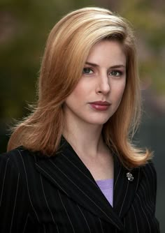 a woman with blonde hair wearing a black suit and purple shirt is looking at the camera