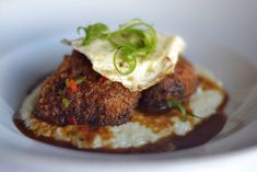 a white plate topped with meat and mashed potatoes covered in gravy, garnished with scallions