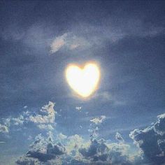 a heart shaped balloon floating in the sky with clouds around it on a sunny day