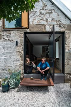 a man and woman sitting on steps in front of a stone building with glass doors