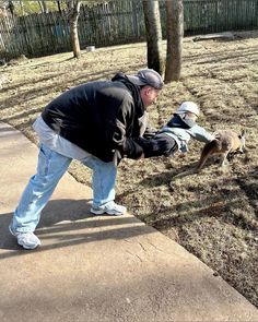 a man bending over to pet a dog on the side of a sidewalk next to a tree