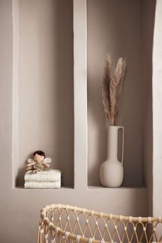 a white vase sitting on top of a shelf next to a basket filled with towels