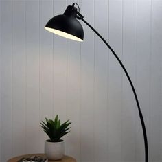 a black floor lamp next to a potted plant on a wooden table in a white room