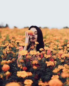 a woman standing in a field of flowers holding her face up to her eye and looking at the camera