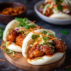 two buns filled with meat and veggies on a cutting board next to bowls of sauce